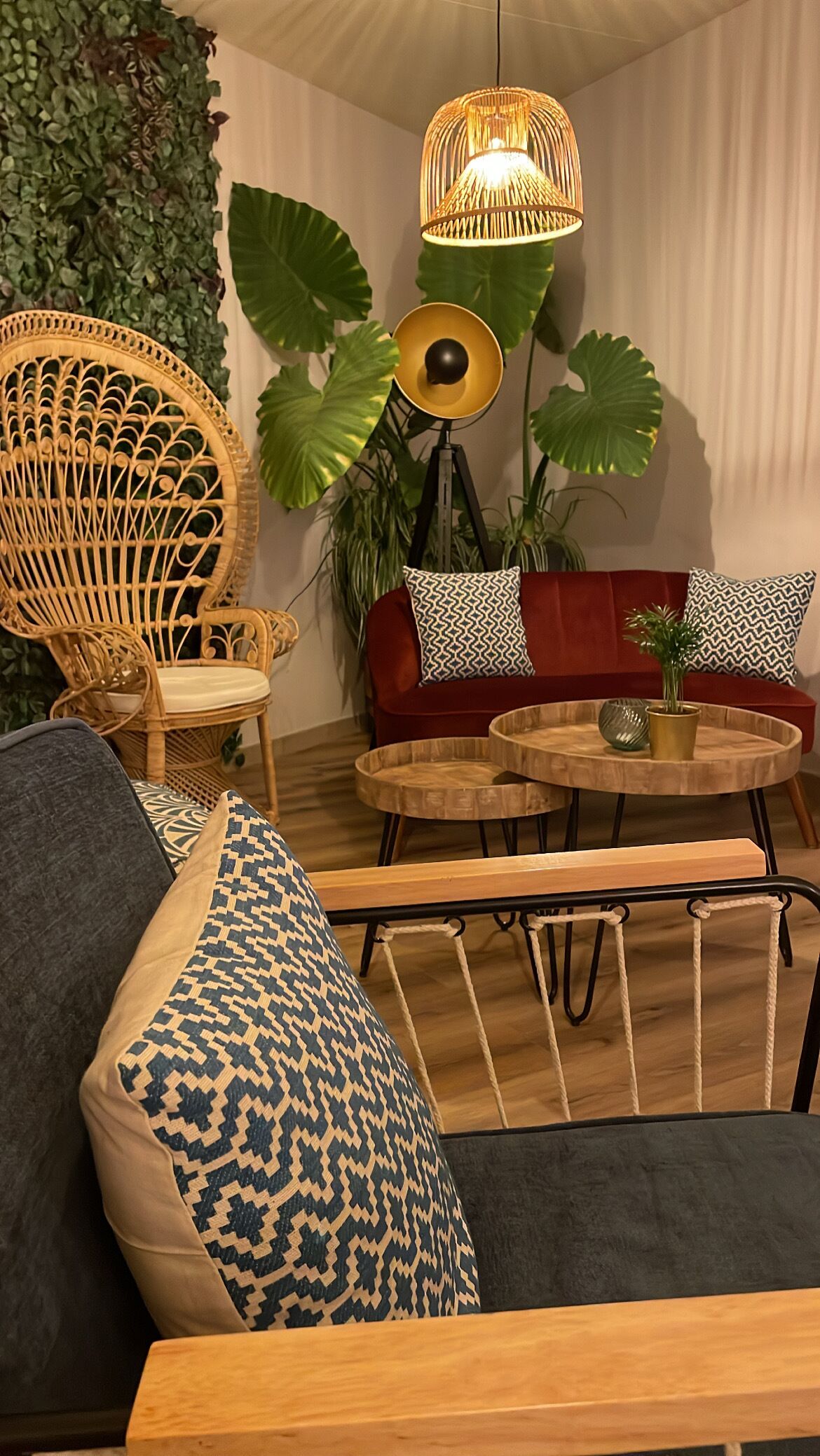 Un rincón acogedor con una silla de mimbre, un sofá rojo y una mesa redonda de madera.
