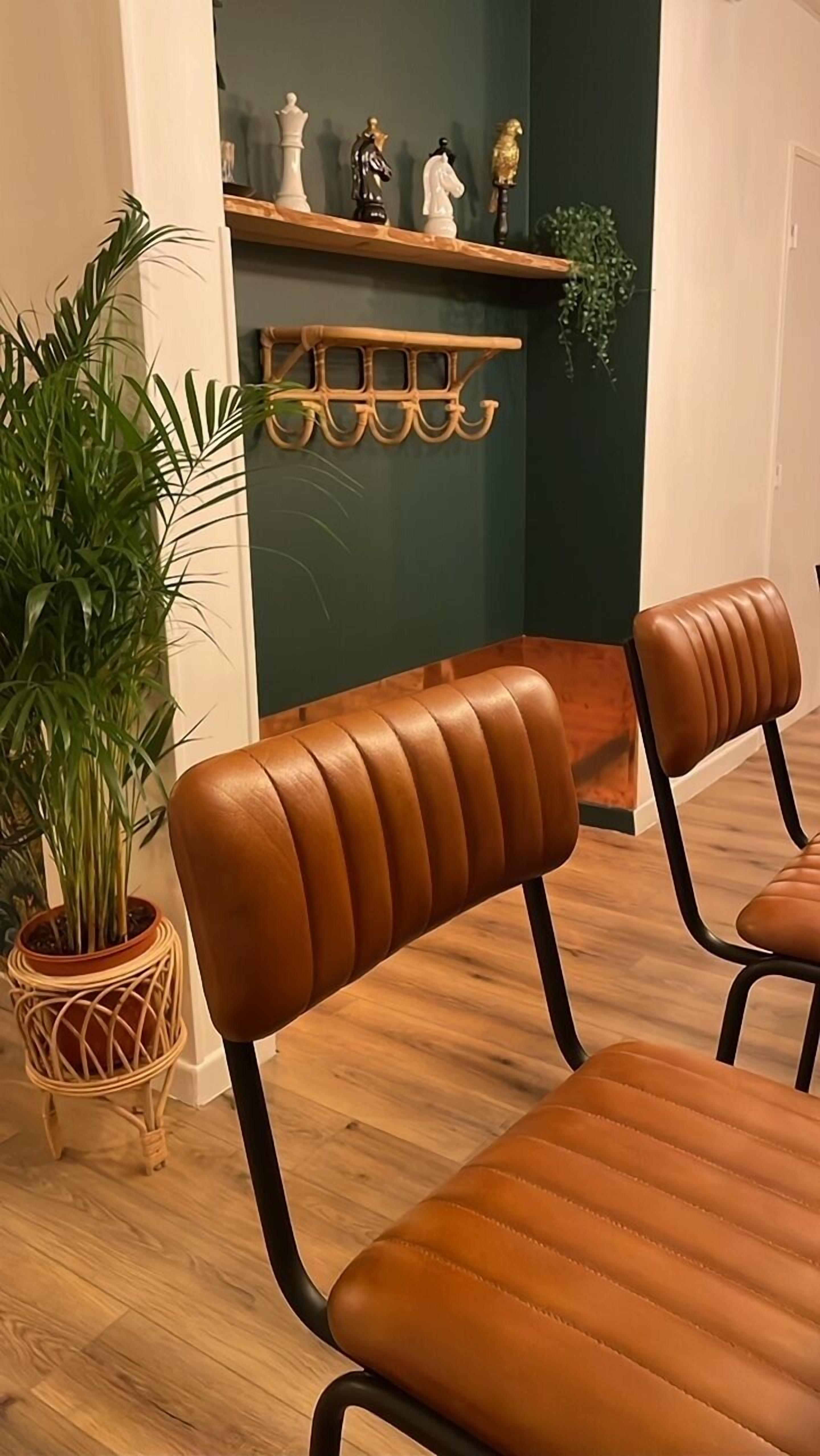 A room with two brown leather chairs, a wooden floor, a green wall, and a shelf with decorative items.