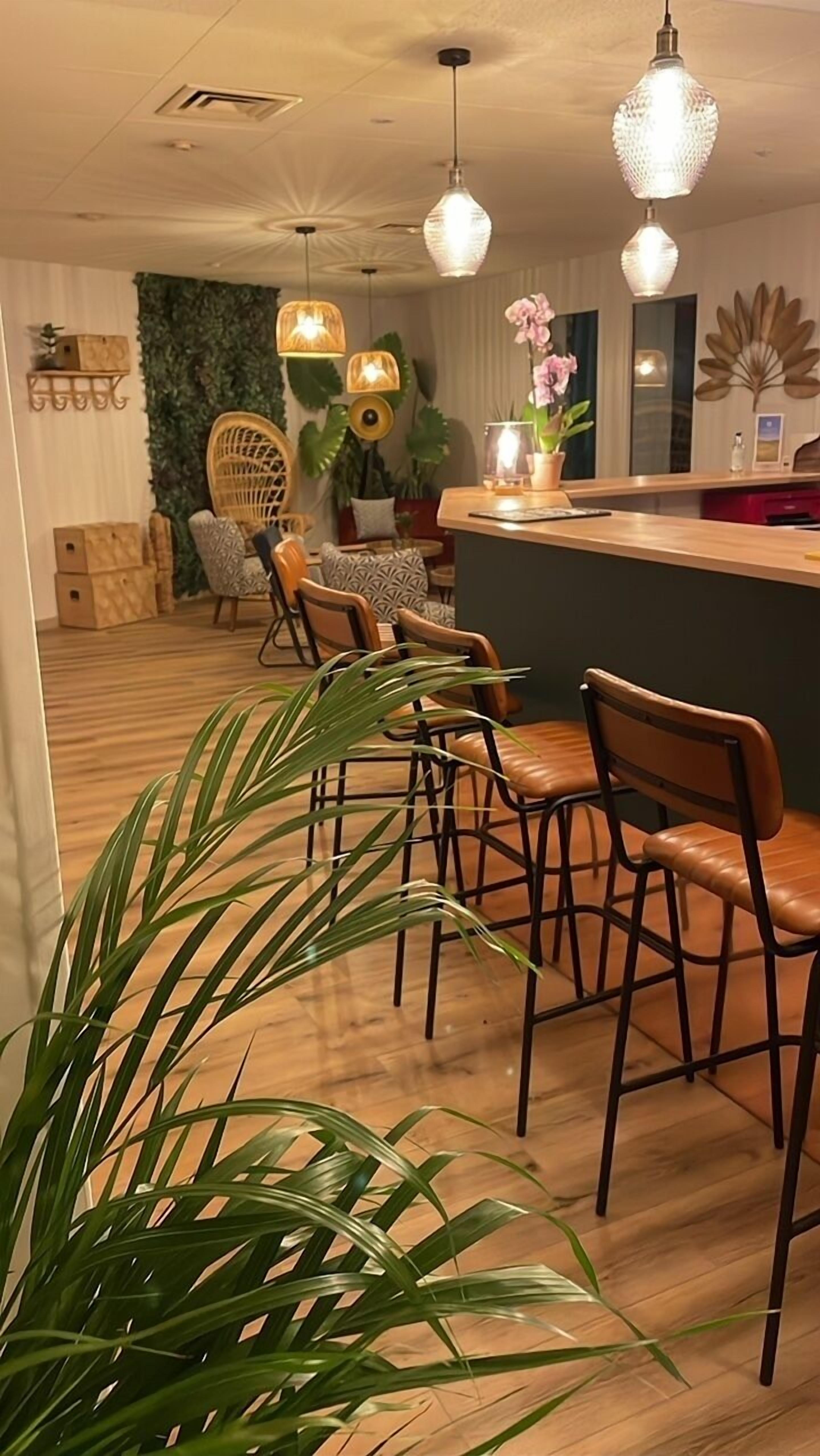 A modern dining area with wooden chairs and a central island, surrounded by potted plants and decorative lighting.