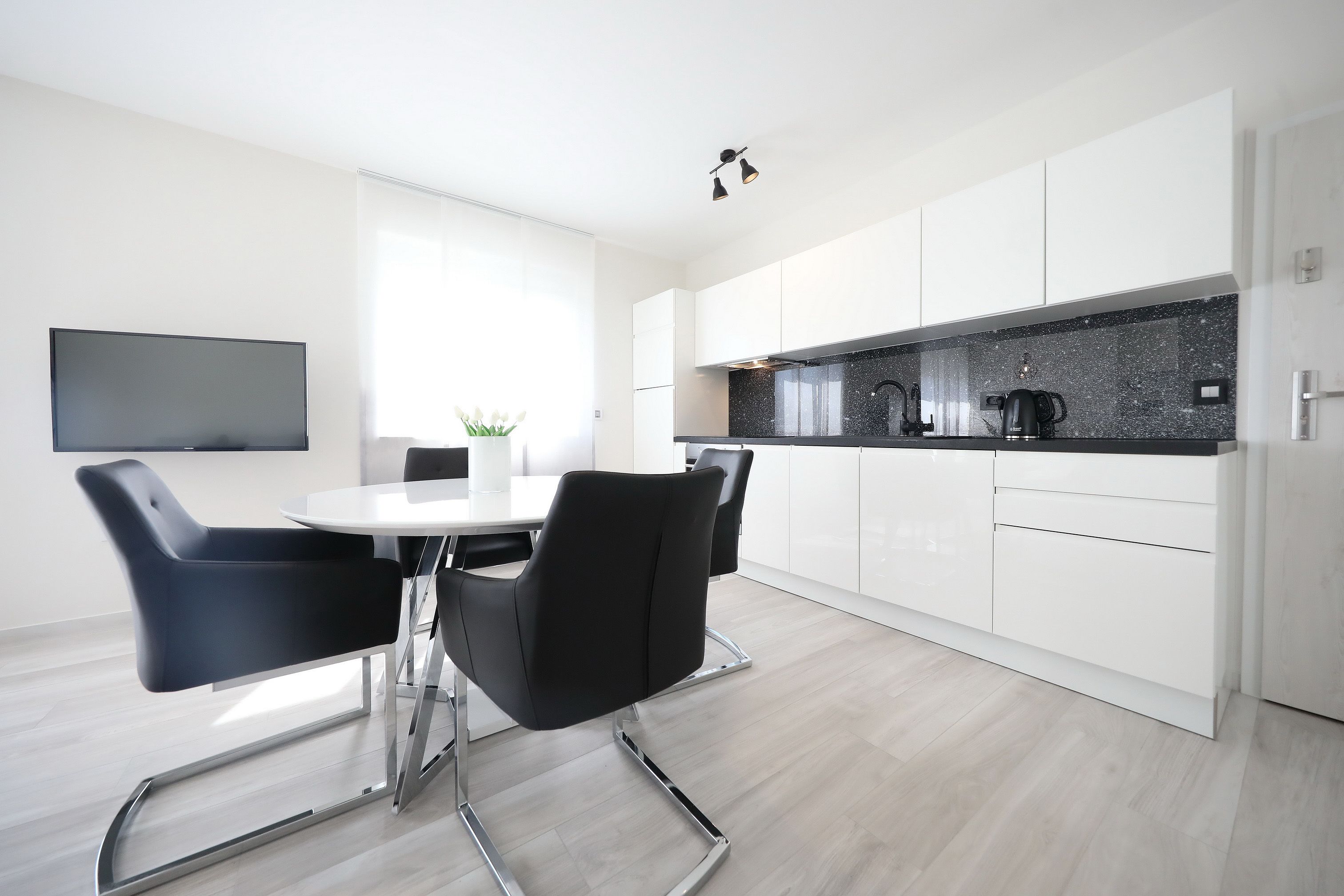 A modern kitchen with white cabinets, a black countertop, and a dining area with black chairs and a white table.