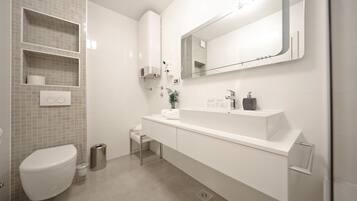 Un baño moderno con un inodoro blanco, un lavamanos con espejo y un cesto de basura.