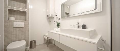 Une salle de bain moderne avec des toilettes blanches, un lavabo surmonté d’un miroir et une poubelle.