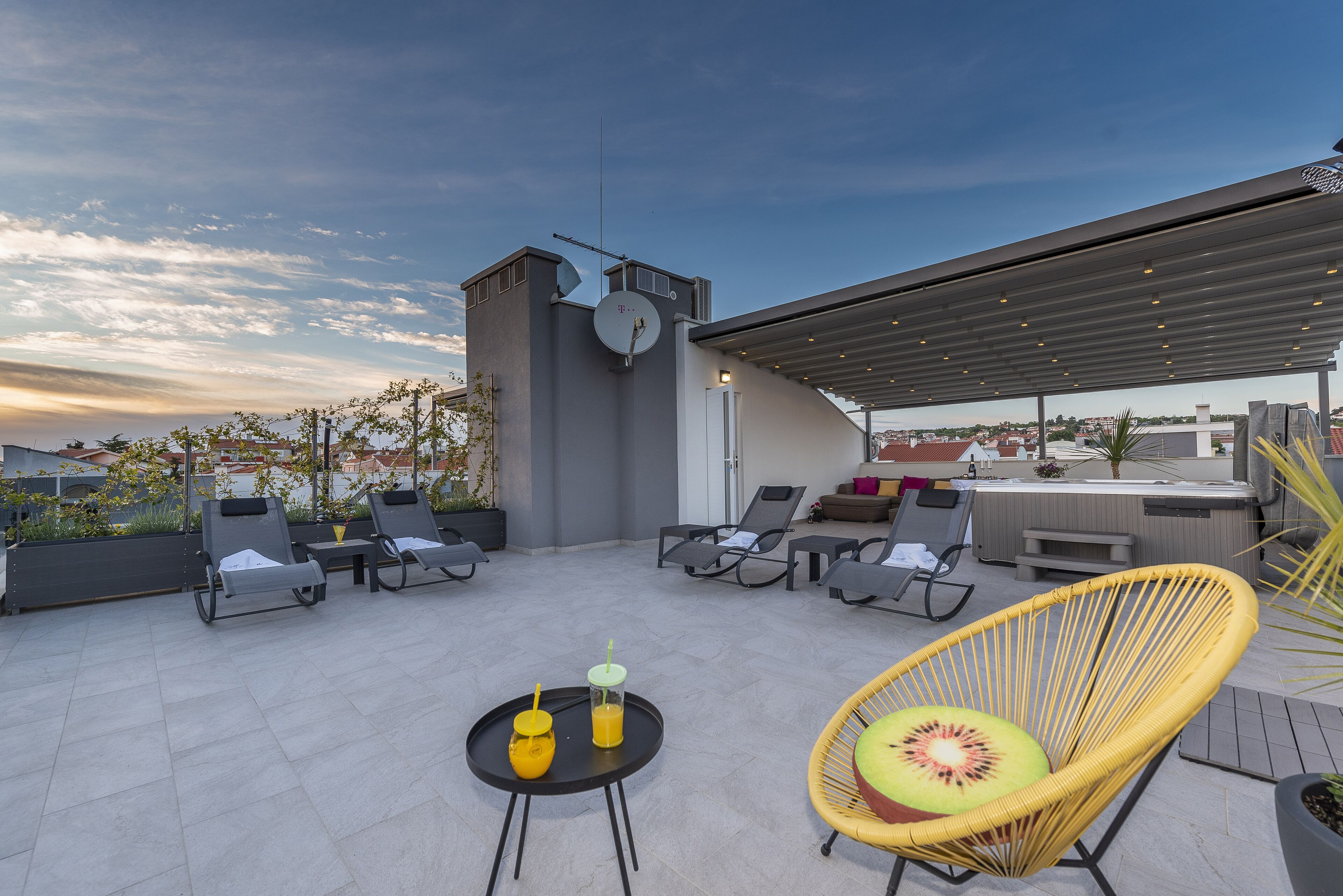 Eine Dachterrasse mit Liegestühlen, einem Esstisch und einem überdachten Bereich.