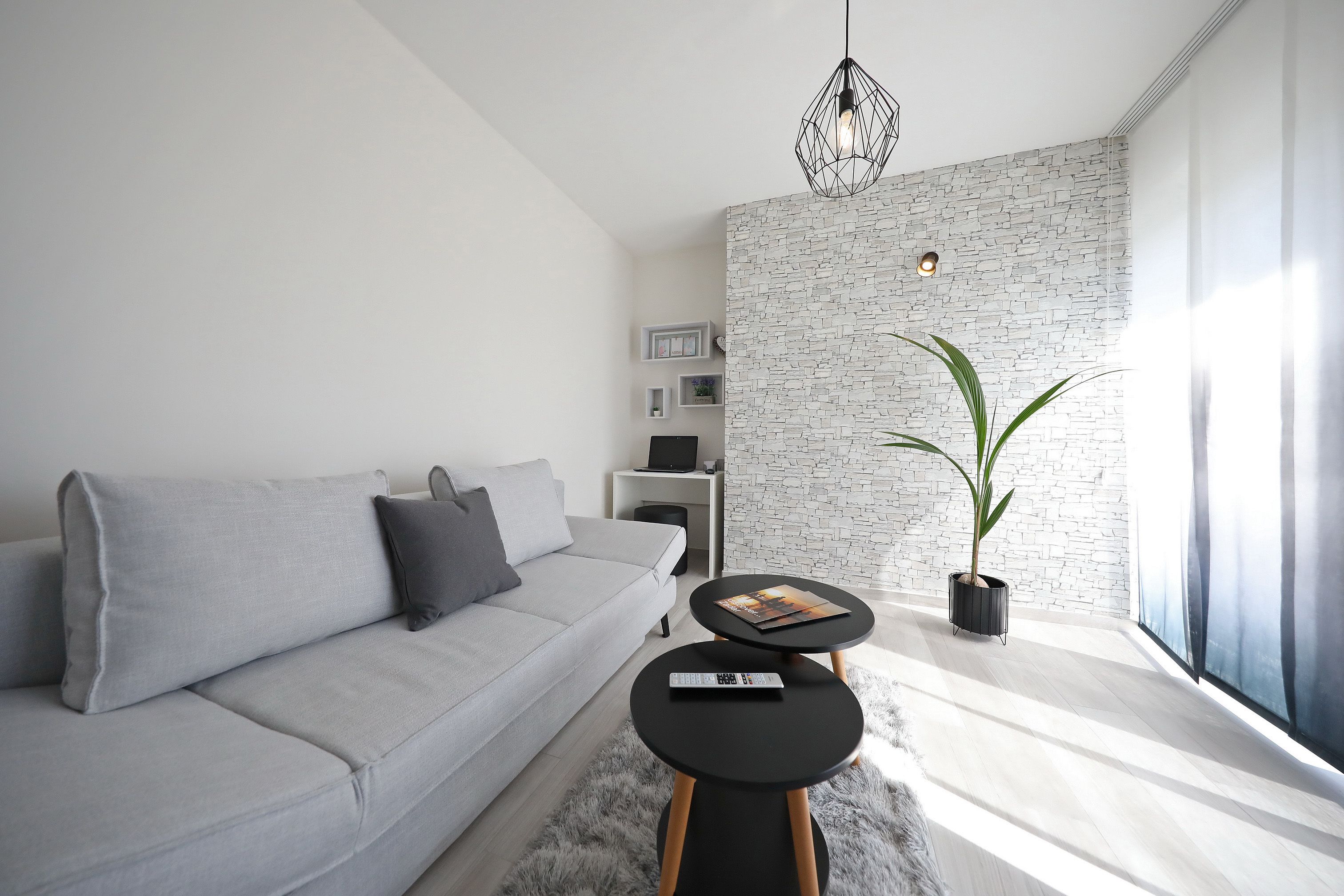A modern living room with a grey sofa, a small round table, a potted plant, and a white brick wall.