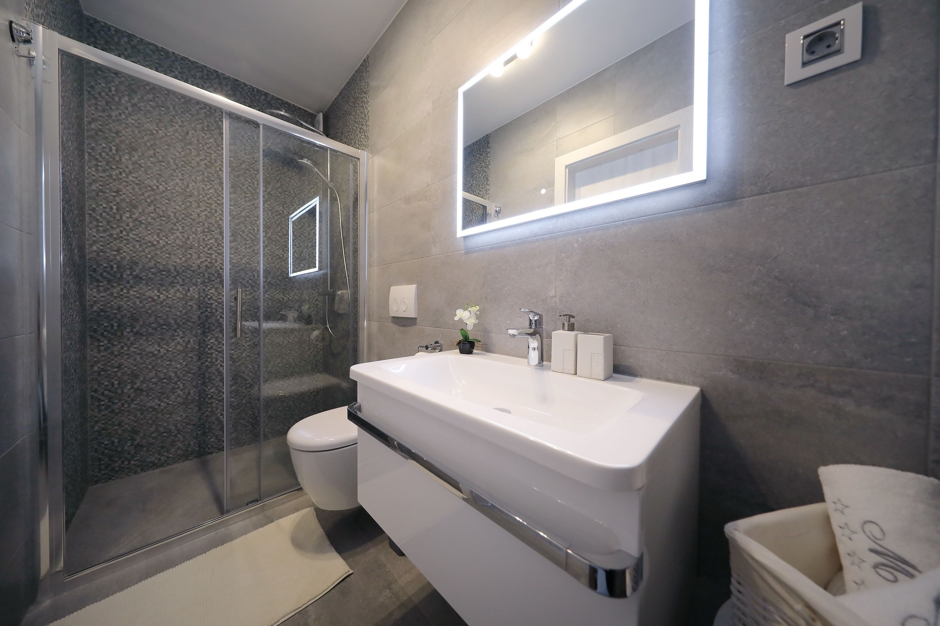 A modern bathroom with a glass-enclosed shower, a white sink, and a large mirror.
