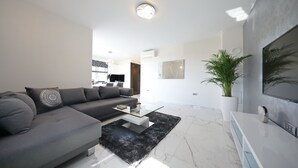 A modern living room with a grey sofa, a glass coffee table, a black rug, and a large potted plant. - Luxury Majpruz Suites (Zadar)