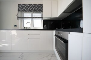 Una cocina moderna con armarios blancos, encimera negra y un ventanal con un valance estampado.