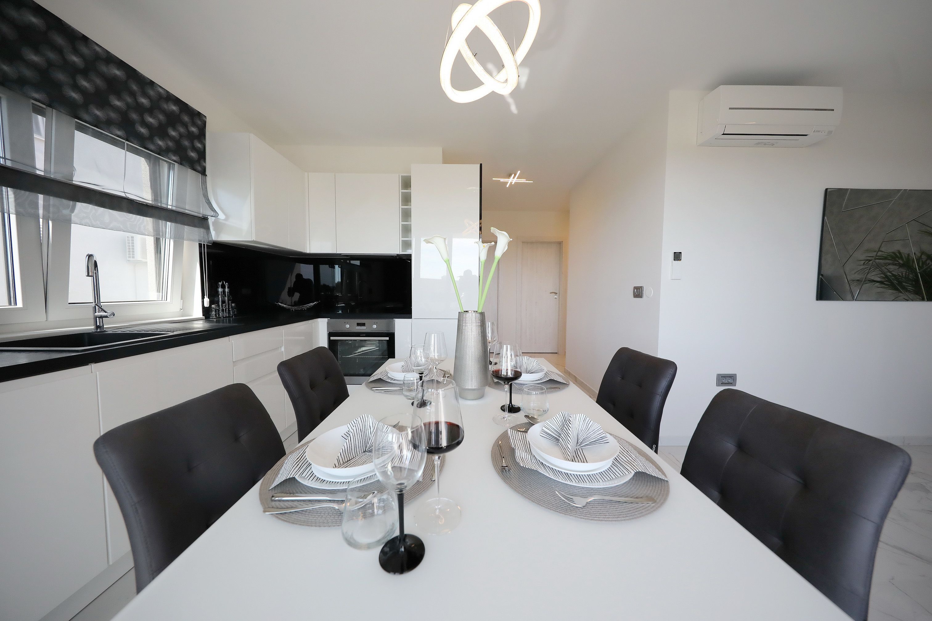 A modern dining area with a white table set for six, black chairs, and a large air conditioning unit on the wall.