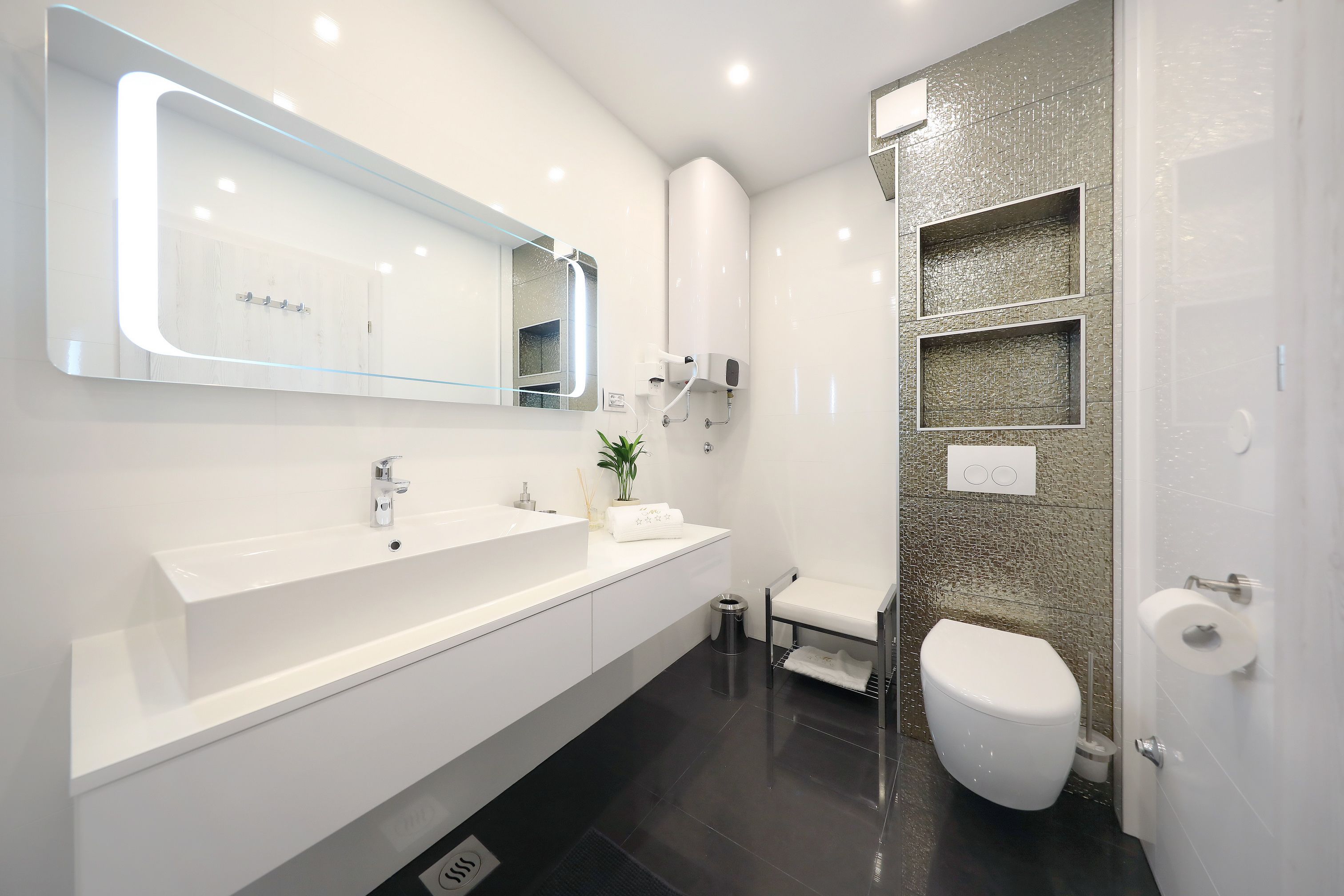 Un baño moderno con un espejo grande, un lavamanos blanco, un inodoro y una zona de ducha.