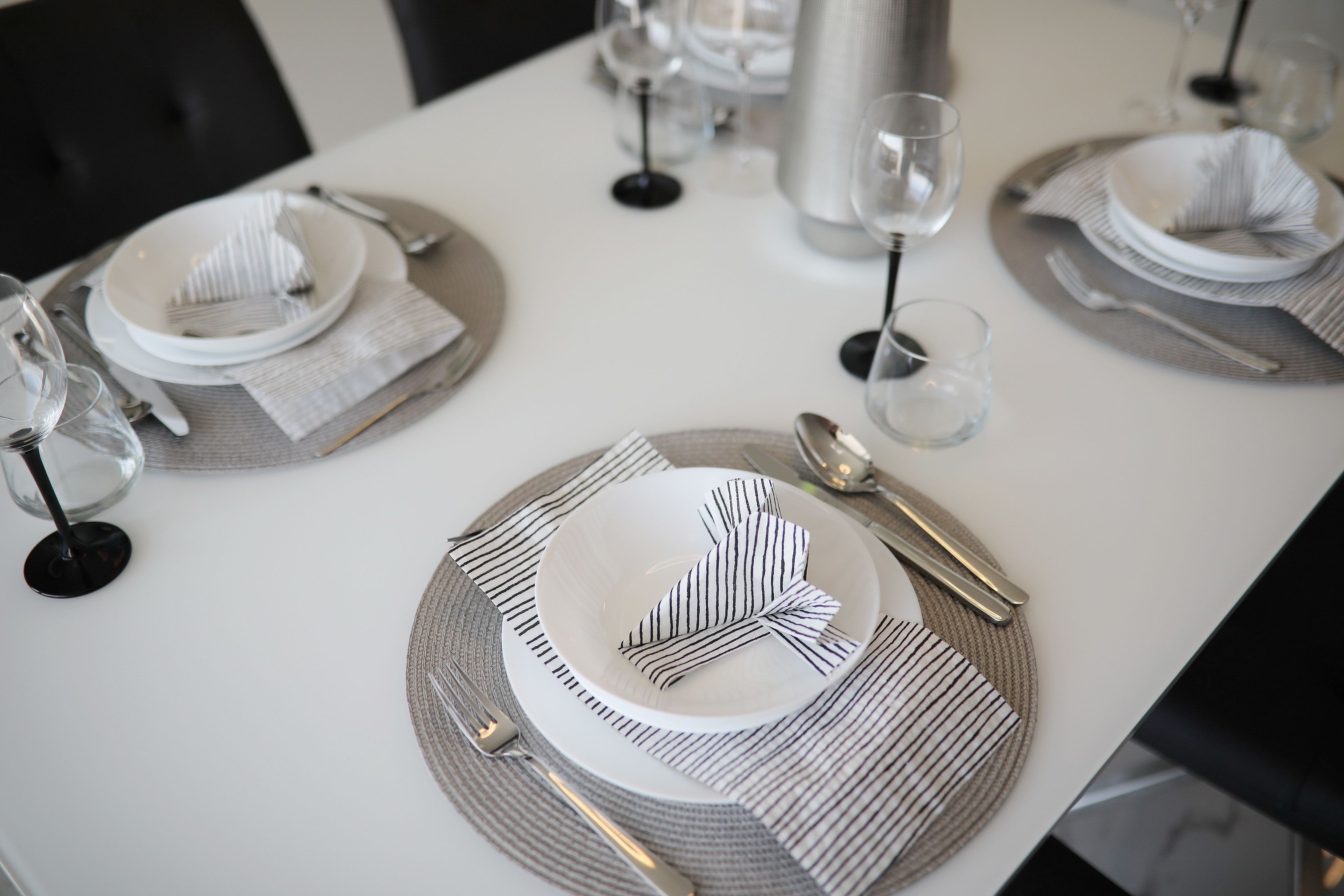 Une table dressée avec de l’argenterie, des assiettes blanches et des verres, le tout disposé sur une nappe blanche agrémentée de sets de table à rayures.