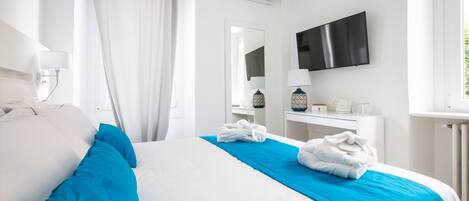 A hotel room with a large bed, a flat-screen TV, a bedside table with a lamp, and a window with curtains.