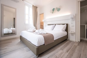 Quarto de hotel moderno com uma cama grande, um espelho, um guarda-roupa e um objeto decorativo na parede.