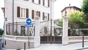 A gated residential area with a white building featuring brown shutters, a blue directional sign, and a black wrought iron gate. - Residenza Elisa (Desenzano del Garda)