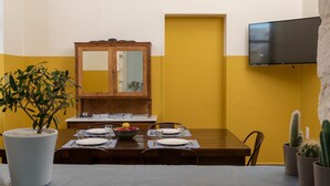 A dining area with a wooden table set for four, a potted plant, and a mirror cabinet. - Intra Muros Hostel (Heraklion)