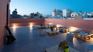A rooftop terrace with wooden furniture, potted plants, and a view of the cityscape. - Intra Muros Hostel (Heraklion)