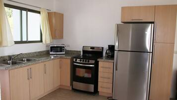 A compact kitchen with a stainless steel refrigerator, a microwave, a stove, and wooden cabinets.