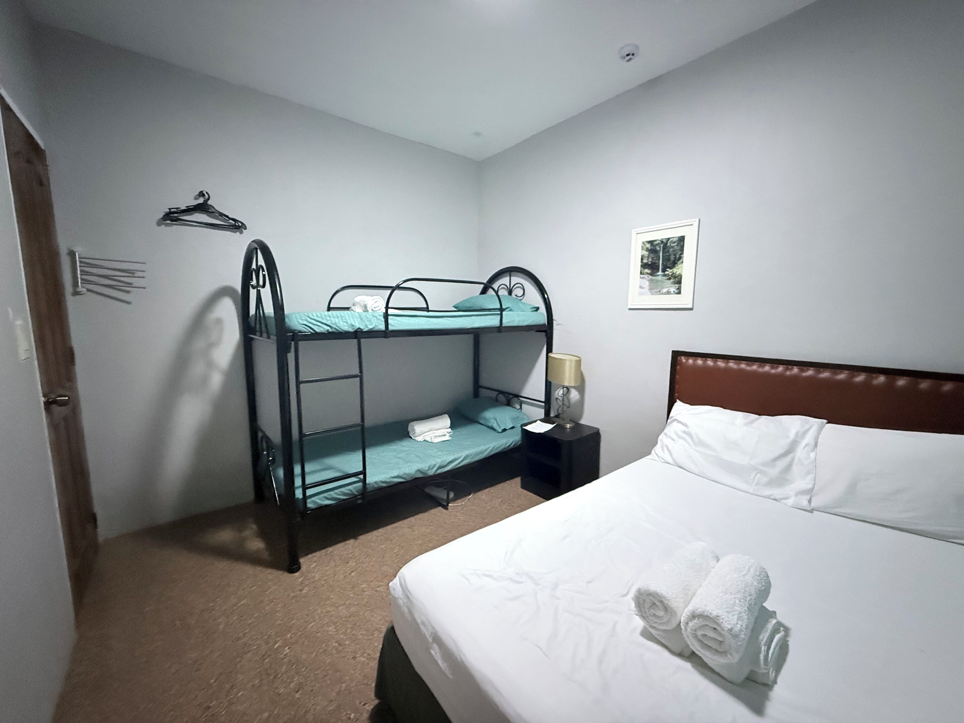 A room with bunk beds, a single bed, a nightstand with a lamp, and a framed picture on the wall.