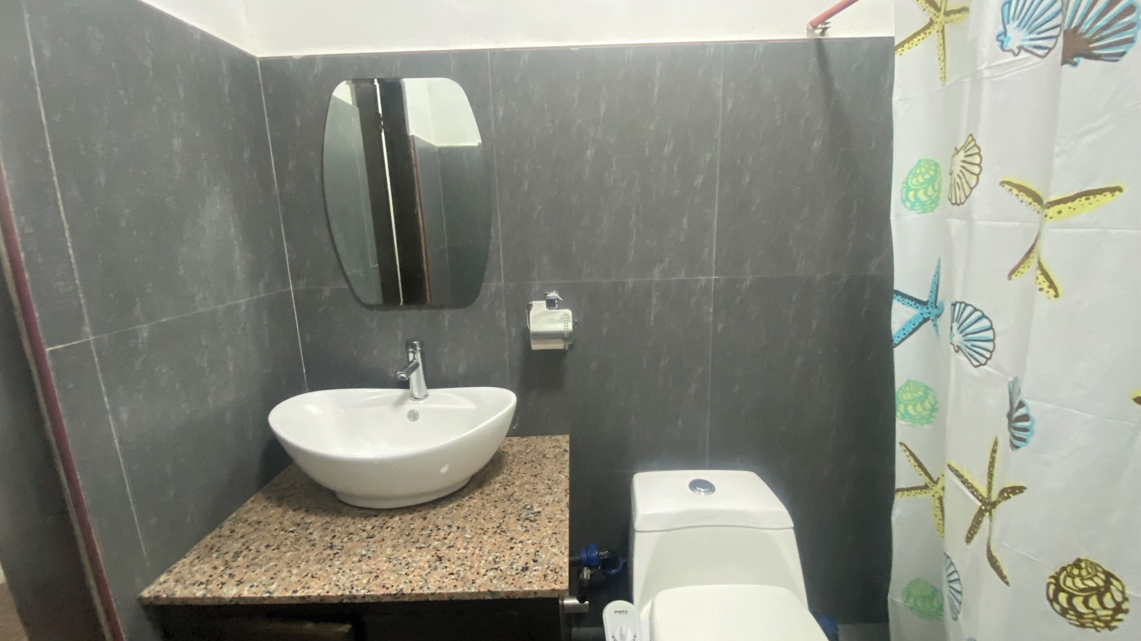 Un baño con un lavamanos blanco, un espejo, un inodoro y una cortina de ducha con estampado de peces.
