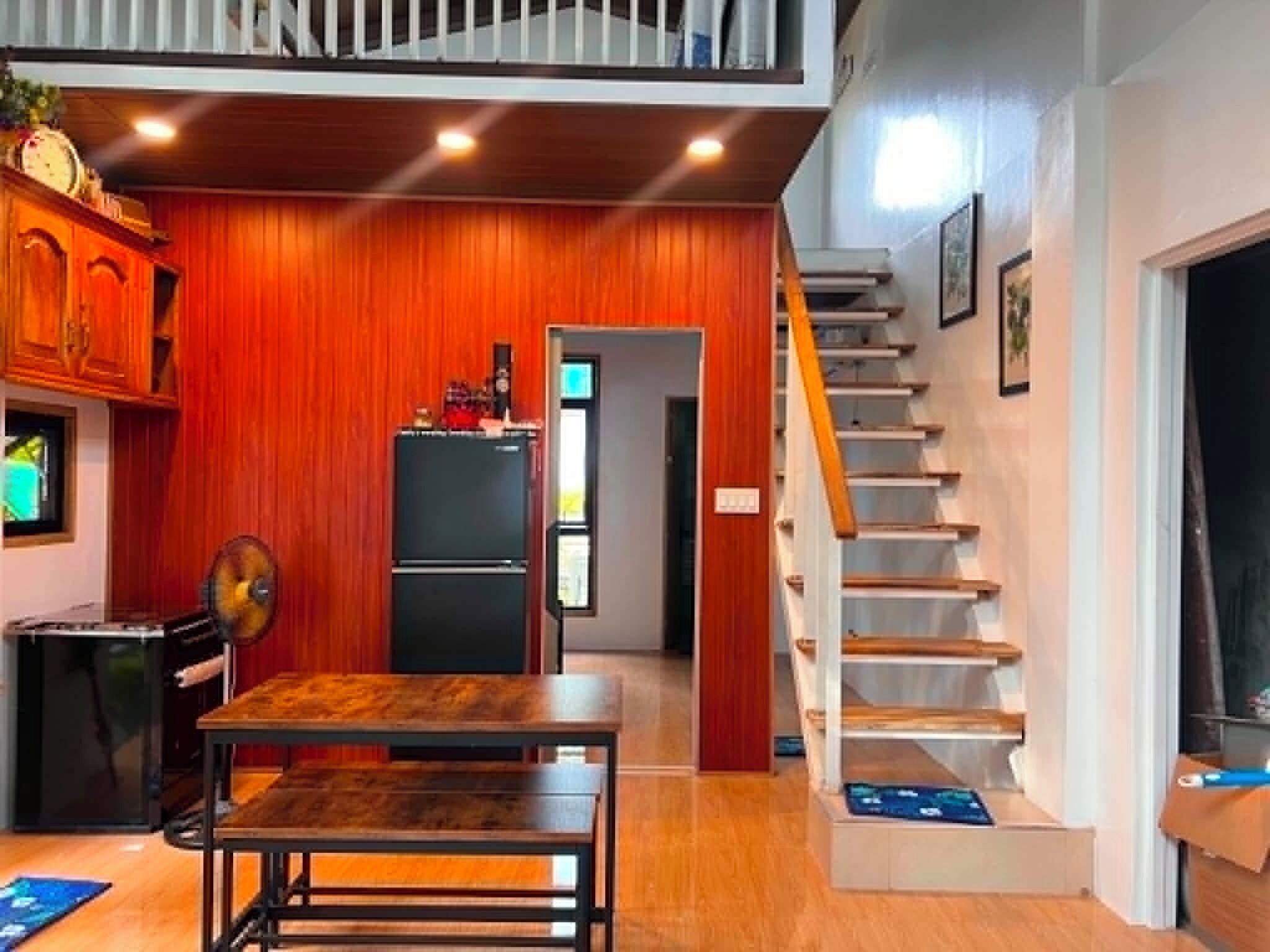 A compact kitchen with wooden paneling, a dining table, a refrigerator, and a staircase.