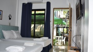 A hotel room with two beds, a desk with a chair, a TV, and a balcony with a green umbrella. - Seaside Travelers Inn by Camiguin Island Home (Catarman)