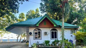 A house with a green roof, a porch, and a garden with various plants. - Seaside Travelers Inn by Camiguin Island Home (Catarman)