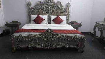 A bed with an ornate headboard, two red pillows, and a white bedspread.