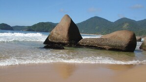 A beach with large boulders and a clear view of the ocean and distant hills. - Pousada Flor de Paraty (Paraty)