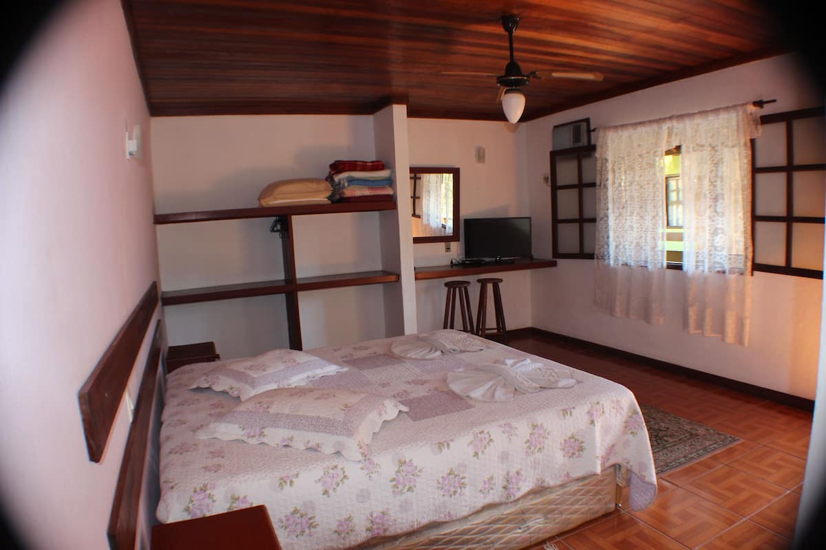 A bedroom with a bed, a desk, a chair, a television, and a window with curtains.