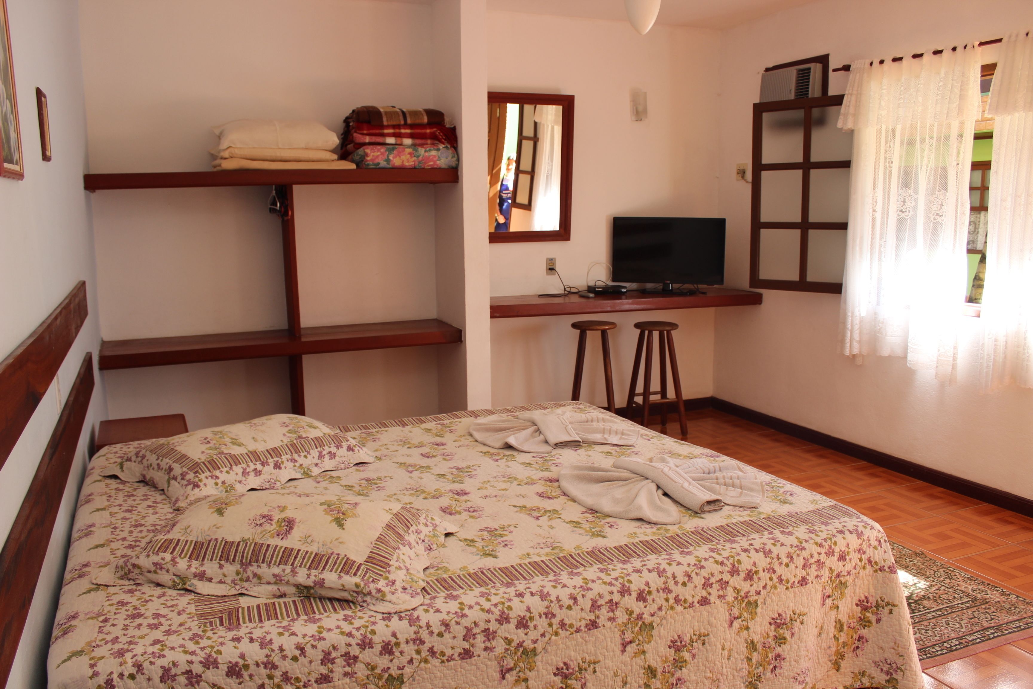 Un dormitorio con cama, escritorio, televisor y ventana con cortinas.