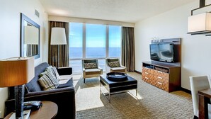 Habitación de hotel con sofá, sillones, una mesita de centro, televisión y vista al océano.