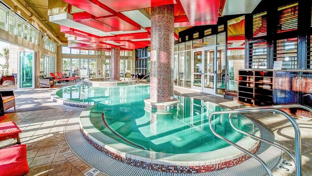 Una amplia piscina cubierta con solárium azulejado, paneles de techo rojos y una columna central.