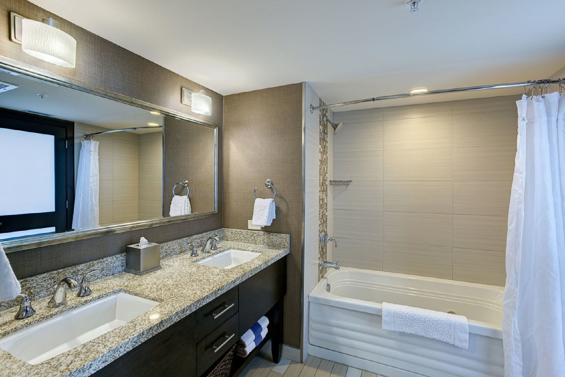 A modern bathroom with two sinks, a large mirror, a bathtub, and a shower curtain.