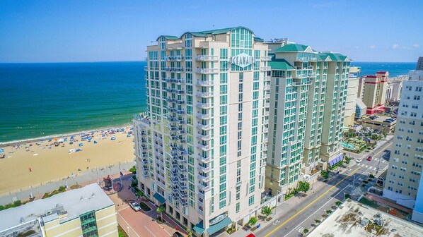A high-rise hotel with multiple balconies, a beach view, and a parking area.