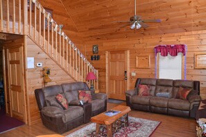 A wooden interior with two brown leather sofas, a wooden coffee table, a ceiling fan, and a staircase. - Cozy Cabin 5 mi 2 Dollywood! Privacy, with the comforts of home! (Pigeon Forge)