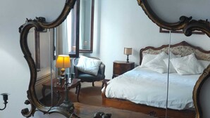 A bedroom with a large ornate mirror, a bed with white linens, a nightstand with a lamp, and a chair. - Ca Vecchio Pozzo:Charming property in central historical Venice (VENICE)