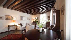A dining area with a round table, chairs, a vase with flowers, and a red patterned rug. - Ca Vecchio Pozzo:Charming property in central historical Venice (VENICE)