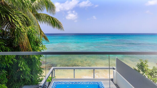 Un balcon donnant sur une mer turquoise et un palmier.