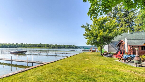 Un chalet au bord du lac, avec un quai, un bateau et une pelouse verdoyante.