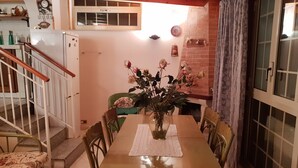 A dining area with a wooden table, chairs, a vase with flowers, a clock, and a refrigerator.