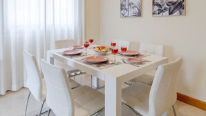 A dining area with a white table, white chairs, a hanging light fixture, and two framed botanical prints on the wall. - Fidalsa Guardamar Resort (Guardamar)