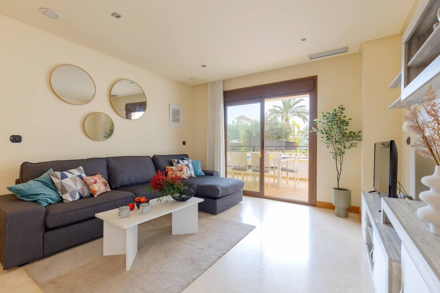 A modern living room with a grey sectional sofa, a white coffee table, and two wall-mounted mirrors.