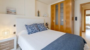 A bedroom with a bed, a nightstand, a wooden wardrobe, and a wall-mounted shelf with decorative items. - Fidalsa Guardamar Resort (Guardamar)