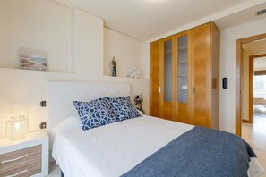 A bedroom with a bed, a nightstand, a wooden wardrobe, and a wall-mounted shelf with decorative items.
