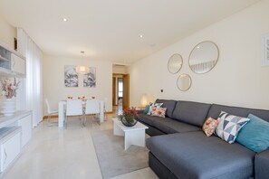A modern living room with a grey sofa, white coffee table, and a dining area with a white table and chairs.