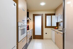 A compact kitchen with a built-in oven, a coffee machine, and a fruit bowl on the counter.