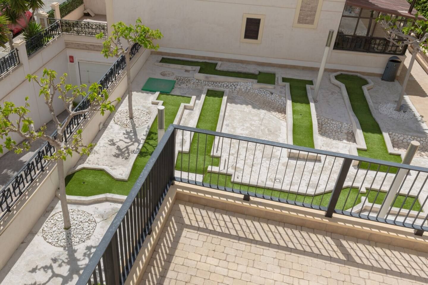 A courtyard with a geometric lawn design, a brick pathway, and a metal railing.