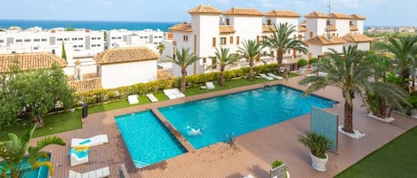 Ein Schwimmbecken mit Liegestühlen, einer Holzterrasse und Blick aufs Meer.
