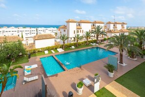 A swimming pool with sun loungers, a wooden deck, and a view of the sea.