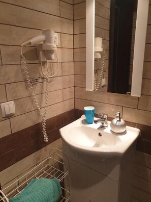 A bathroom with a white sink, a blue cup, a hairdryer, and a mirror.