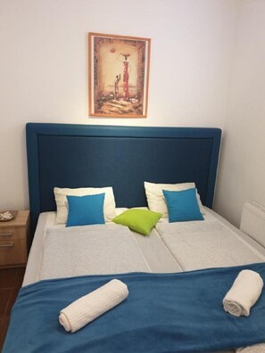 A neatly made bed with blue and white bedding, two pillows, and two rolled towels.